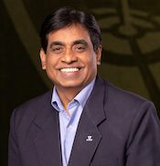 A man with dark hair, wearing a navy blazer and light blue shirt, smiling at the camera against a dark, blurred professional background. Sourcing, Procurement, 3rd Party Risk