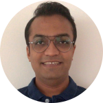 A person with short dark hair, wearing round glasses and a blue collared shirt, is smiling confidently in front of a plain light background. Sourcing, Procurement, 3rd Party Risk