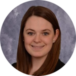 A woman with straight brown hair, wearing a black top, smiles confidently at the camera against a gray and white mottled background. Sourcing, Procurement, 3rd Party Risk