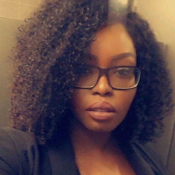 A woman with curly dark hair, wearing glasses and a black blazer, looks at the camera with a neutral expression. The blurred indoor background adds a professional touch. Sourcing, Procurement, 3rd Party Risk