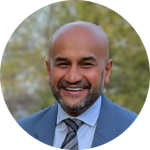 A smiling, bald man with a beard, dressed in a blue suit, white shirt, and striped tie, stands outdoors with trees softly blurred in the background. Sourcing, Procurement, 3rd Party Risk
