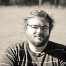 A man with glasses and a beard sits outdoors, wearing a striped sweater. The black-and-white image features a blurred background and subtle texture. Sourcing, Procurement, 3rd Party Risk