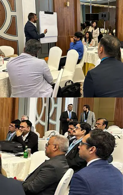A man stands at a flip chart presenting to a group of professionals seated at round tables in a formal conference room. Attendees listen attentively, some taking notes and others facing the speaker during the business meeting. Sourcing, Procurement, 3rd Party Risk