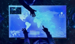 Two people point at a large digital touchscreen displaying a glowing blue world map with data overlays, highlighting technology and innovation. Sourcing, Procurement, 3rd Party Risk