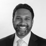 A man with short dark hair and a beard, wearing a suit and tie, smiles at the camera against a plain light background, exuding confidence. Sourcing, Procurement, 3rd Party Risk