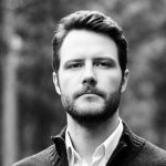 Black and white portrait of a man with a beard wearing a collared shirt and sweater. Sourcing, Procurement, 3rd Party Risk