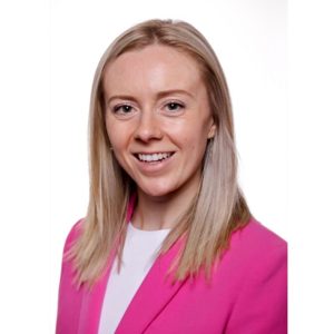Smiling woman with straight blonde hair wearing a bright pink blazer over a white top, photographed against a plain white background. Sourcing, Procurement, 3rd Party Risk