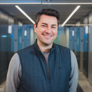 A man with dark hair smiling at the camera, wearing a gray long-sleeved shirt and a patterned vest. Sourcing, Procurement, 3rd Party Risk